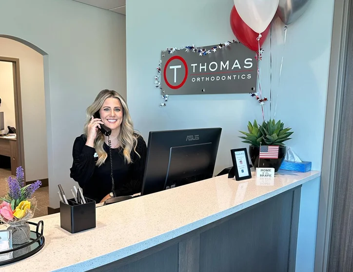 Receptionist answering phone at Thomas Orthodontics office desk.
