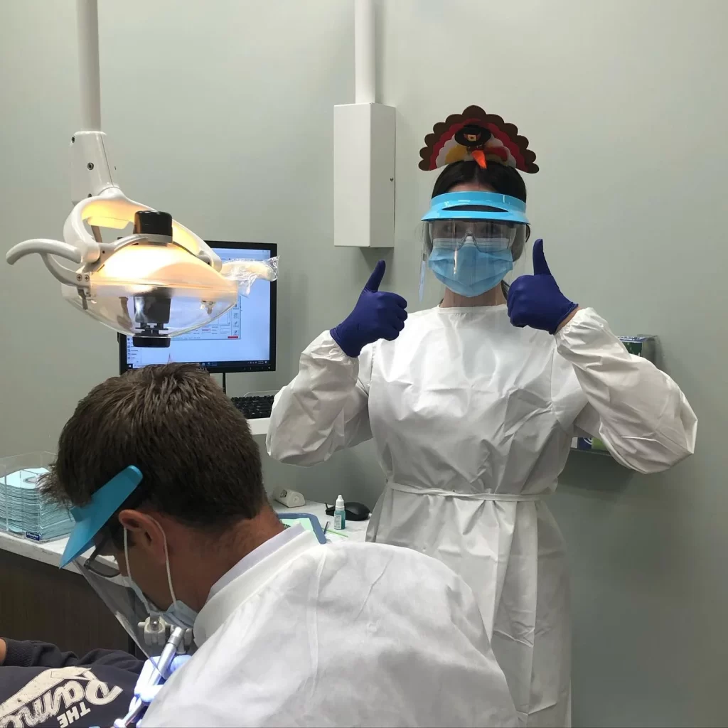 Dentist in PPE giving thumbs up in clinic.